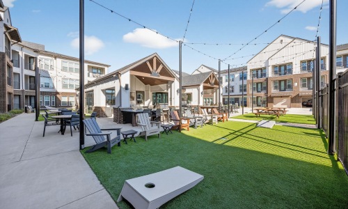 Outdoor community amenity space at Aspire at Sherman featuring lounge seating, grilling areas, lawn games, and string lights.